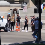 Sean Feucht at the bottom of the Capitol stairs looking on while a queer coded presentation is given by someone who reserved the space before his group of Christian nationalists